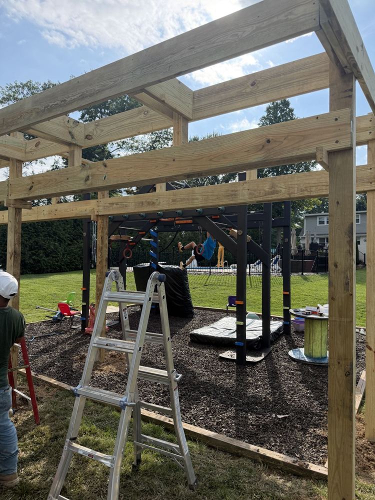 Overhead timber beams set across the posts of a backyard ninja rig, a ladder below