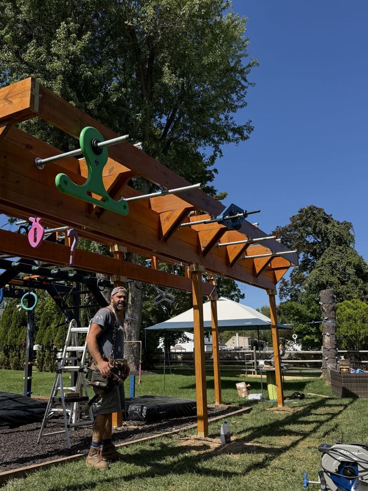 Builder standing under a finished stained rig hung with green, pink and blue grips