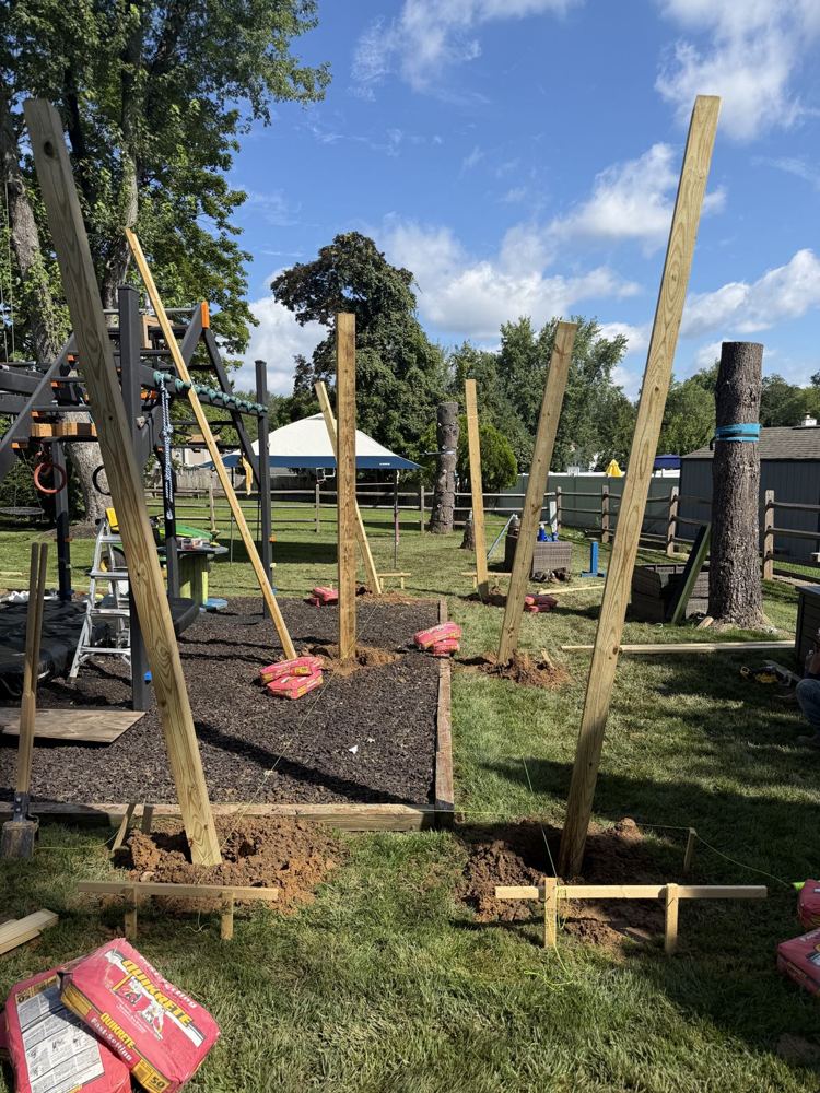 Wooden posts braced upright in a backyard on day one of a ninja rig build
