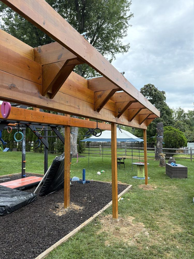 Freshly stained ninja rig with angled braces, rings and grips beside a rubber-mulch training area
