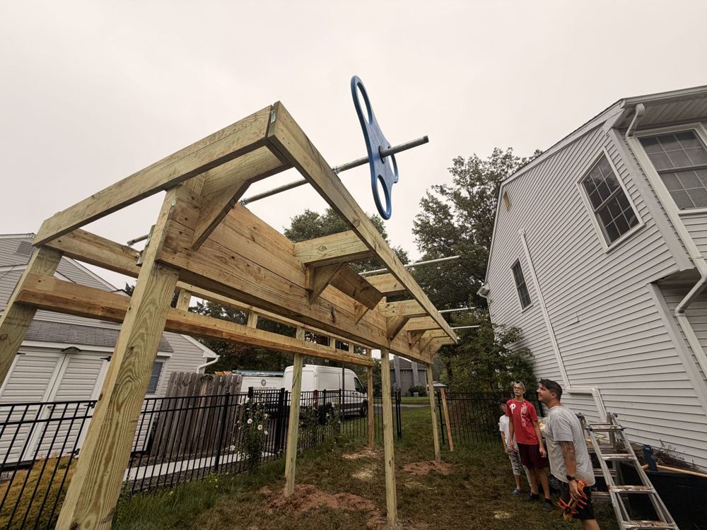 Natural wood ninja rig frame with angled corner braces and steel crossbars beside a house