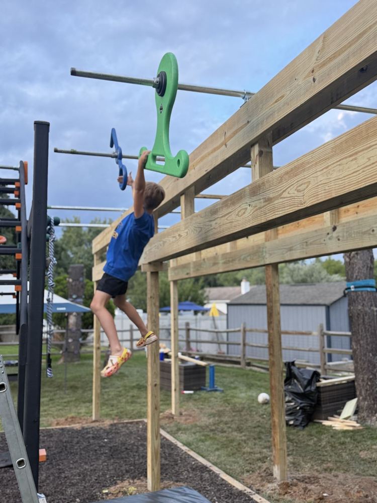 Young ninja swinging from a green spinning grip on a newly built backyard rig