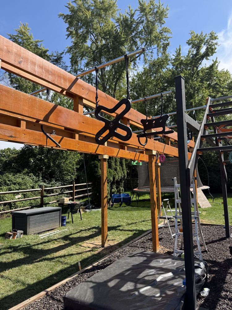 Stained ninja rig loaded with black hanging grips on steel bars above a crash mat